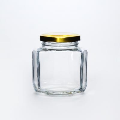 China Eco-friendly Flint Blank Glass Food Container High Oval Hexagonal Glass Jar With Gold Metal Hook Lid For Jam for sale