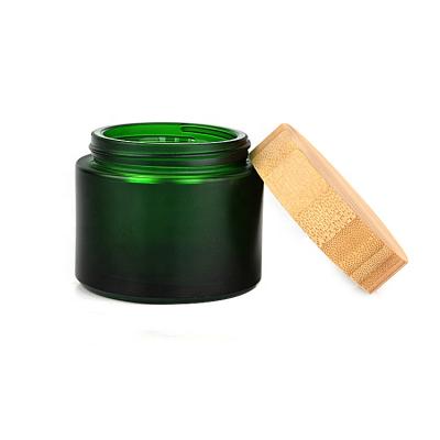 China 100ml cosmetic wholesale bamboo lid frosted dark green glass cosmetics jar glass cream jar with bamboo lid for sale