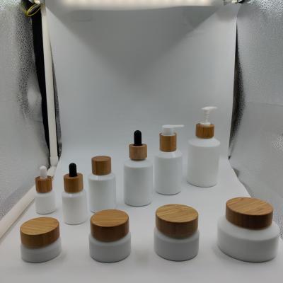 China Fashionable cosmetic packaging shoulder glass opal white oblique bottle and jar with bamboo/wooden lid and white plastic dropper for sale